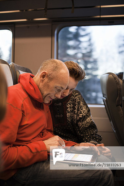 Mann und Jugendlicher benutzen Tablet im Zug
