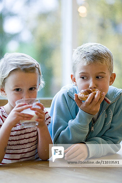 A boy and a girl drinking milk and eating rolls.