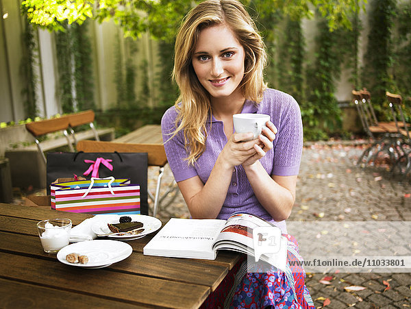 Eine junge Frau trinkt draußen in einem Café Kaffee.