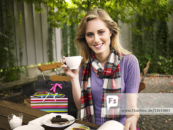 Eine lächelnde junge Frau in einem Cafe draußen.