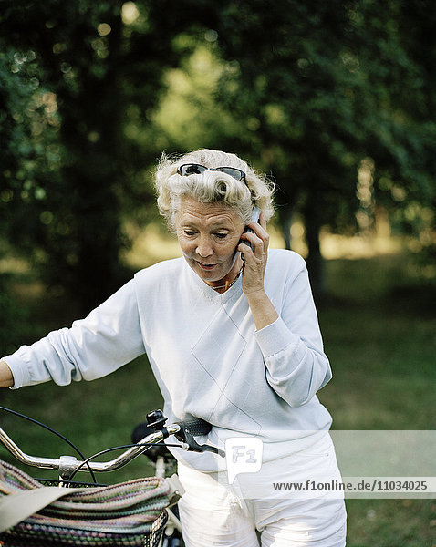 Ältere Frau mit Fahrrad  die in ein Handy spricht