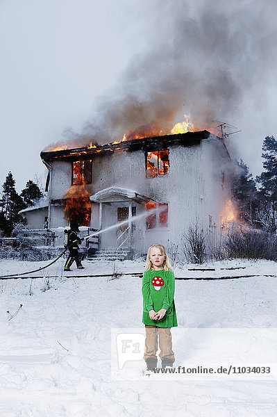 Mädchen vor einem brennenden Gebäude  Feuerwehrmann im Hintergrund