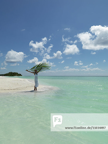 Frau hält Palmwedel am tropischen Strand