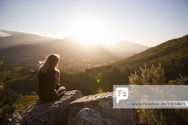 Frau sitzt auf einem Berg und betrachtet den Sonnenuntergang