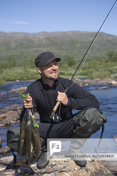 A man holding a casting rod and fish  Tarnaby  Sweden.