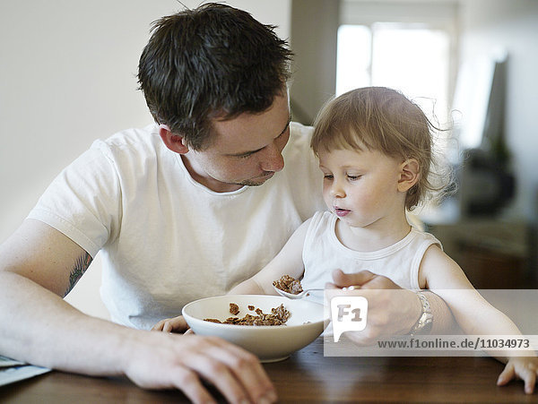 Ein Mädchen  das auf dem Schoß seines Vaters sitzt und isst  Schweden.