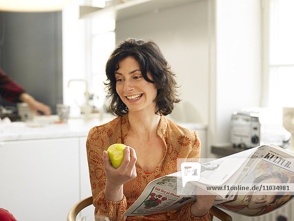 A woman with a newspaper and an apple.
