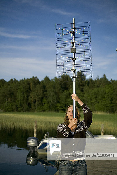 Eine Frau hält eine digitale Fernsehantenne in den Schären  Schweden.