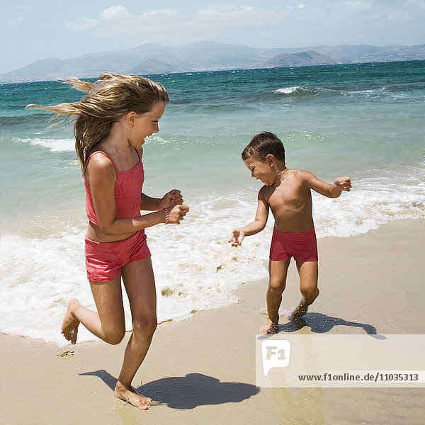 A brother and sister running on a beach.