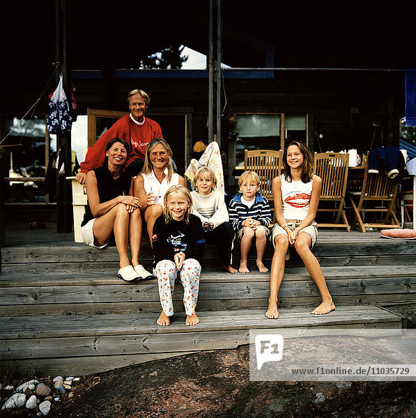 Eine Familie mit Freunden sitzt vor einem Haus  Schweden.
