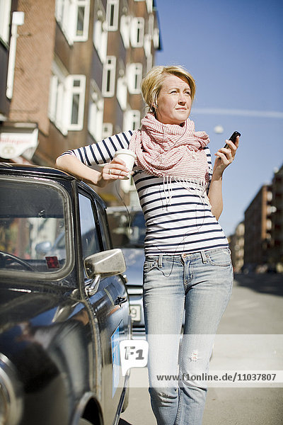 Frau benutzt ein Mobiltelefon neben einem Auto  Schweden.