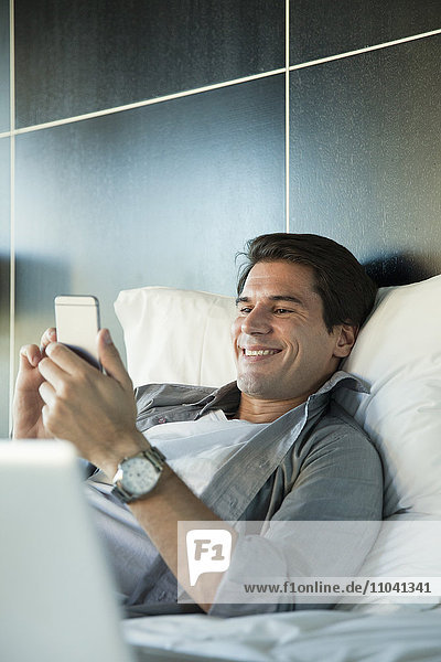 Mann entspannt im Bett mit Multimedia-Smartphone
