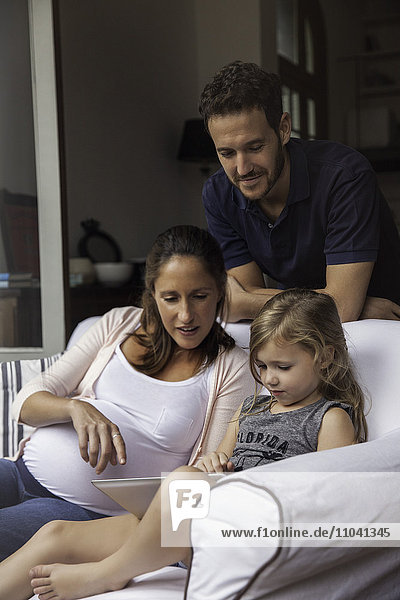 Vater schaut auf als Mutter und Tochter verwenden digitale Tablette zusammen