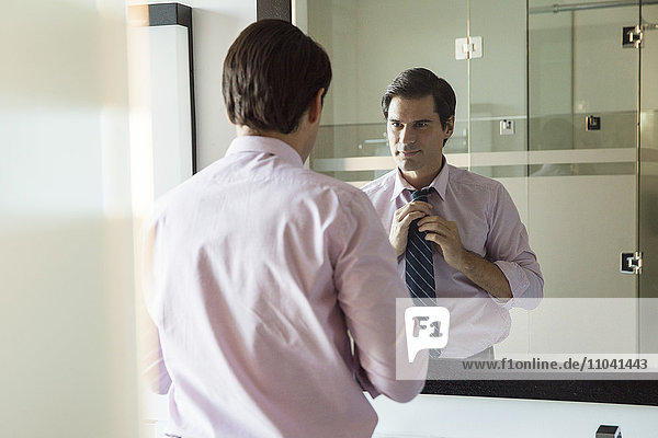 Man looking in bathroom mirror  adjusting necktie