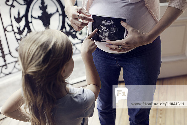Mutter mit Ultraschallaufnahme zur Vorbereitung der Tochter auf die bevorstehende Ankunft eines neuen Geschwisterkindes
