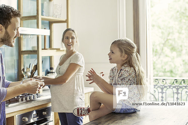 Girl chatting with parents preparing family meal in kitchen