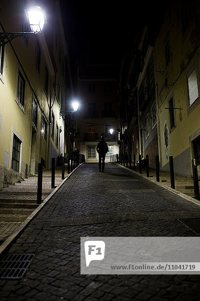 Ein Mann  der nachts auf der Kopfsteinpflasterstraße läuft.