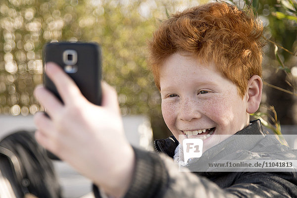 Junge  der ein Smartphone benutzt  um einen Selfie zu nehmen.