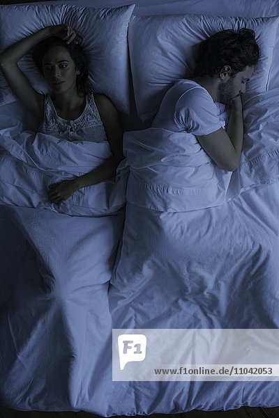 Frau liegt wach neben dem schlafenden Ehemann.