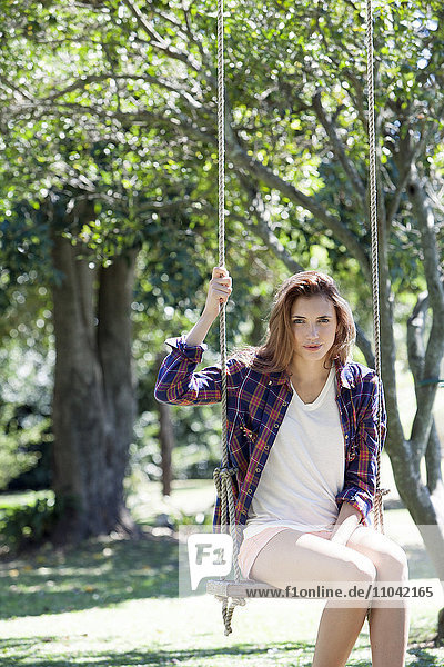 Young woman sitting on swing in park  portrait