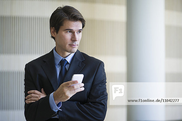 Businessman using smartphone  looking away in thought