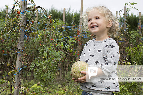 Kleines Mädchen mit Melone im Garten