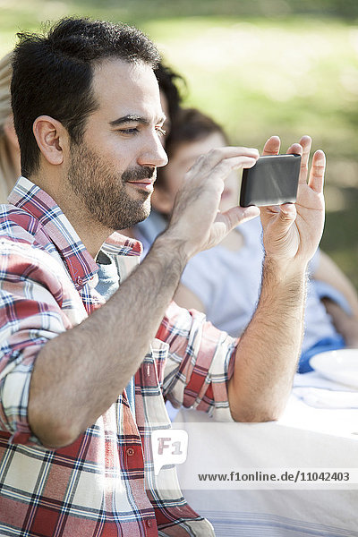 Mann beim Fotografieren mit dem Smartphone beim Treffen mit Freunden