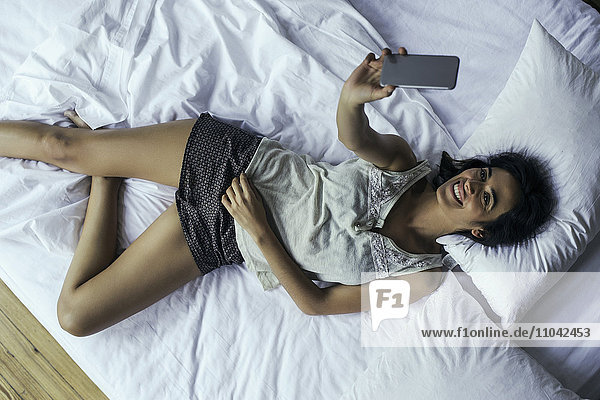 Frau  die auf dem Bett liegt und Selfie mit Smartphone nimmt