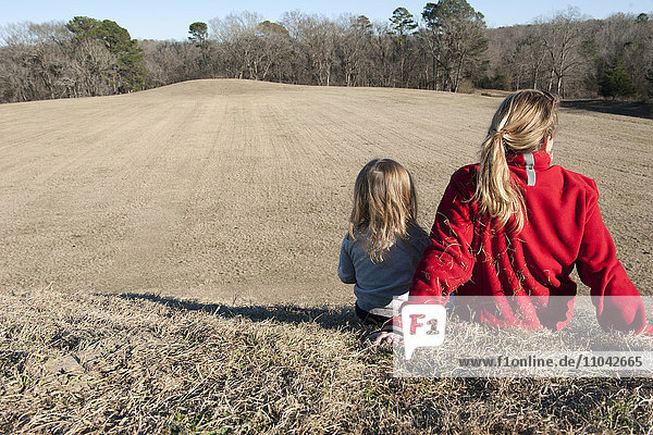Mother and daughter sitting together on hill  rear view