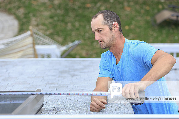 Gehörloser kaukasischer Dachdecker beim Ausmessen eines Oberlichts auf dem Dach