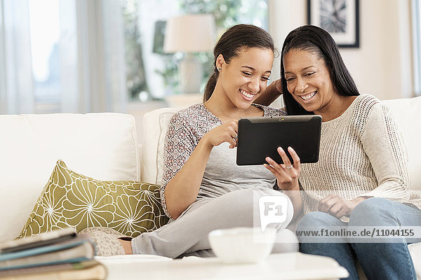 Mutter und Tochter benutzen ein digitales Tablet auf dem Sofa