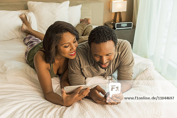 Couple using digital tablet and cell phone on bed