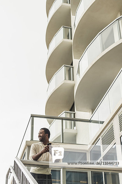 Schwarzer Mann benutzt Mobiltelefon auf Balkon