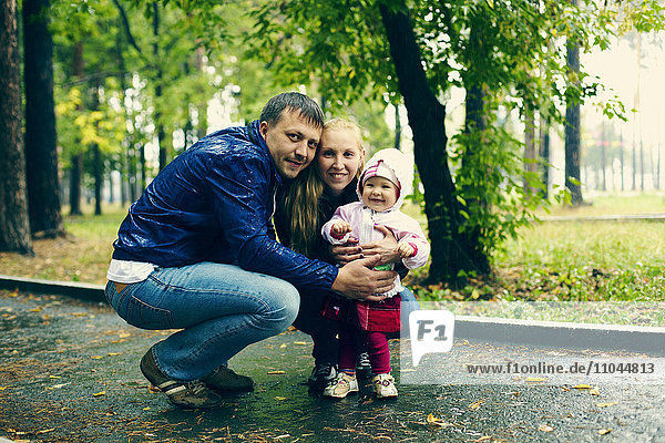 Kaukasische Familie lächelnd auf regnerischem Weg im Park