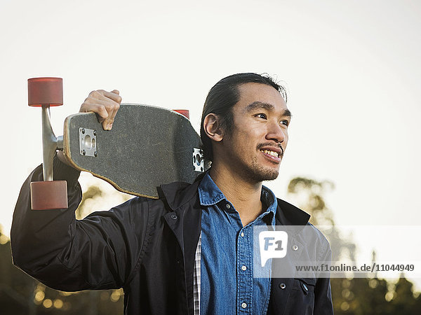 Chinese man carrying skateboard outdoors