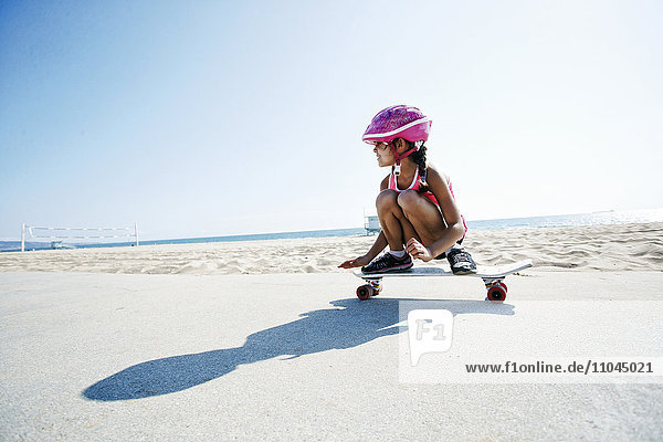 Mixed race girl riding skateboard at beach