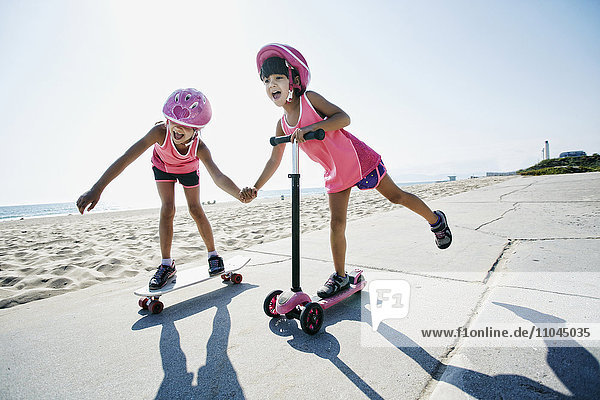 Girls riding skateboard and scooter at beach