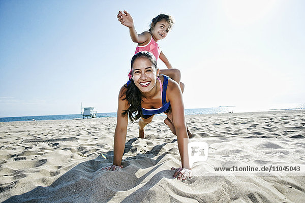 Mother doing push-ups with daughter at beach