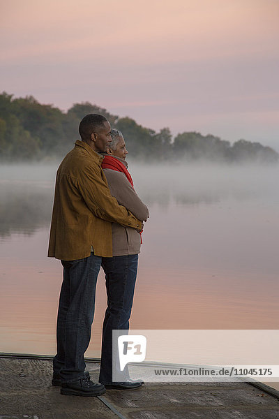 Älteres Paar umarmt am nebligen Fluss bei Sonnenaufgang