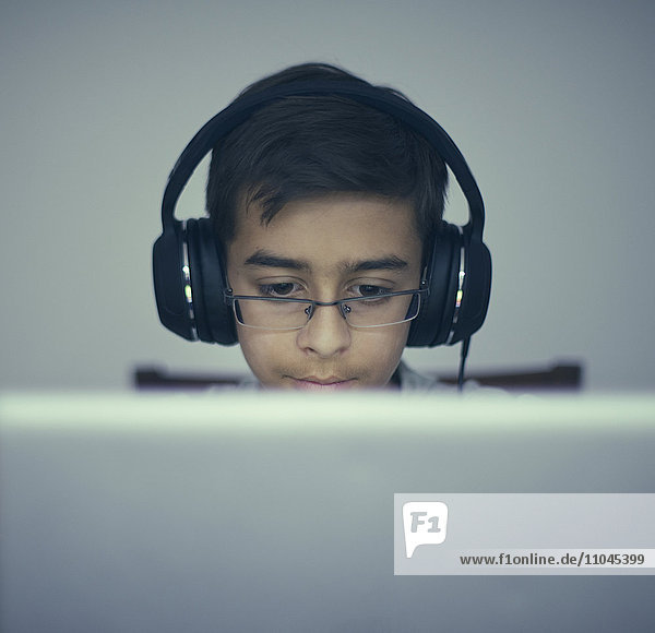 Gemischtrassiger Junge hört mit Kopfhörern am Laptop