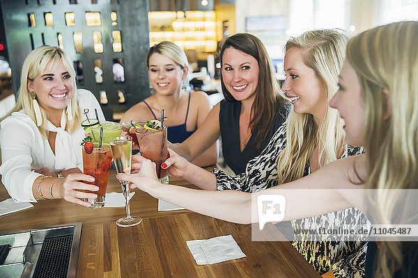 Caucasian women toasting at bar with cocktails
