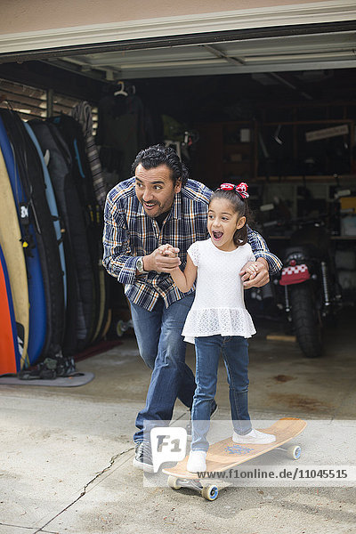 Hispanic father teaching daughter to ride skateboard