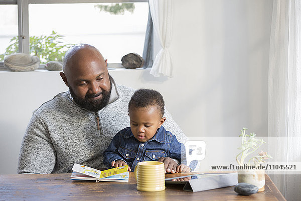 African American father and son reading book at table