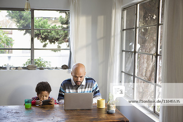 Gemischtrassiger Vater und Sohn nutzen Technik am Tisch