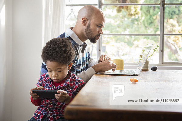 Gemischtrassiger Vater und Sohn nutzen Technik am Tisch