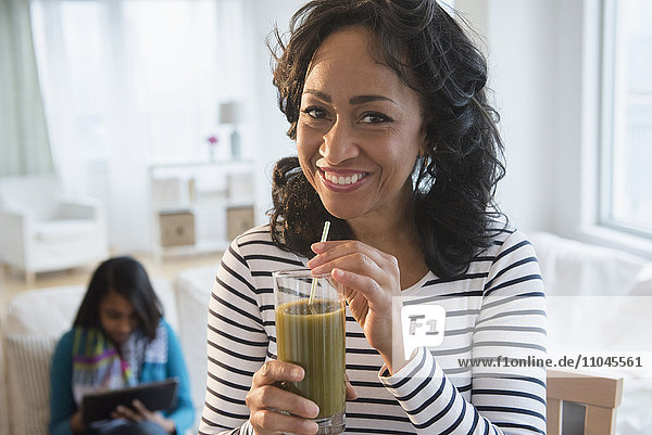 Mother drinking green smoothie while daughter uses digital tablet