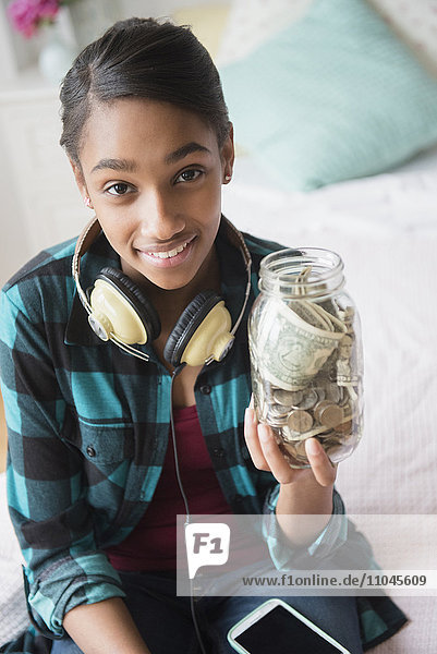 Mixed Race girl holding jar containing cash and coins