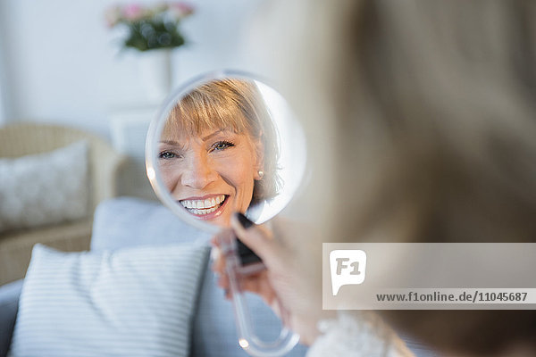 Older Caucasian woman smiling in handheld mirror