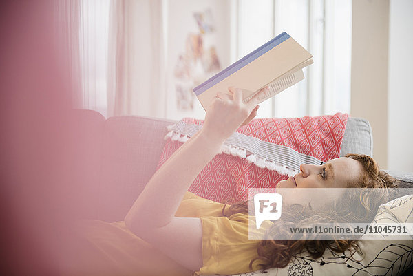 Kaukasische Frau liegt auf dem Sofa und liest ein Buch