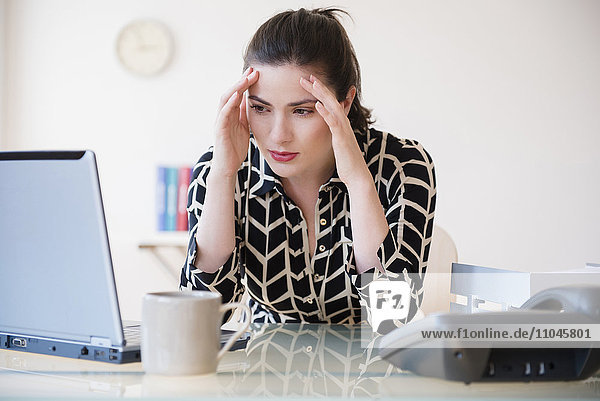 Kaukasische Geschäftsfrau mit Kopfschmerzen am Laptop